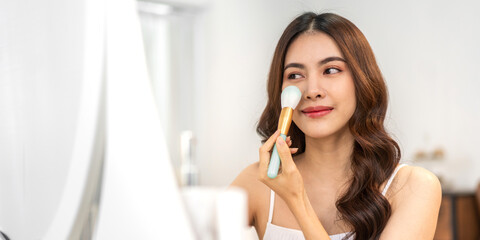 Smiling of young beautiful pretty asian woman clean fresh healthy white skin looking at mirror.asian girl holding make-up brushes and make up on face with cosmetics set at home.facial beauty 
