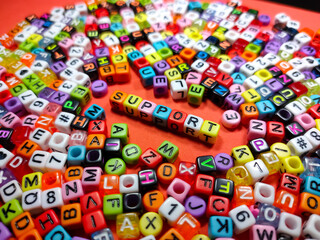 Selective focus.Colorful dice with word SUPPORT on red background.Shot were noise and film grain.