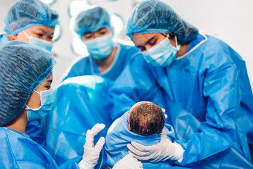 Professional anesthesiologist doctor medical team and assistant is performing baby cesarean section and hold the baby giving birth with surgery equipment in modern hospital operation room