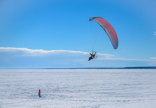 A motor paraplane flies over a frozen lake for a girl walking in the snow