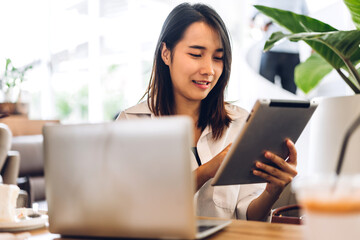 Portrait of smiling happy beautiful asian woman relax using technology of laptop computer sitting on chair.Young hipster asian girl freelancer business thinking with new idea content in cafe