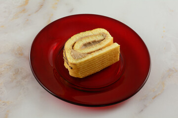 Slice of tiramisu coffee cream cake roll on red glass plate on table