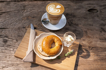 Breakfast bagels with cream cheese in a plate and hot coffee in a glass placed on a wooden table. 