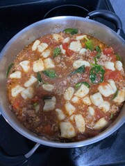 homemade gnocchi in large cooking pot with tomato sauce and spinach