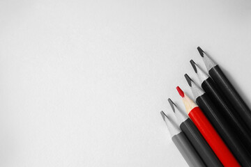 Bright red pencil on a background of dark pencils. Color highlight accents. Red versus gray. Colored pencils for drawing on a light background