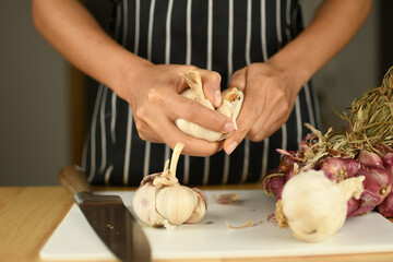 hands of a person with red onion and garlic picking on white board in the kitchen