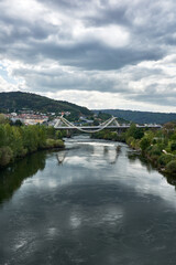 A cityscape with view of the Millenium Bridge on the Minho River seen from the Roman Bridge in the picturesque medieval city of Ourense in Galicia, Spain, on a cloudy spring day.