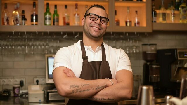 portrait of a confident smiling bartender at the bar in a restaurant with a tattoos on his hands