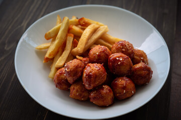 Spicy coated meatballs with spicy sauce served with fried potatoe fries. Korean style snacking.