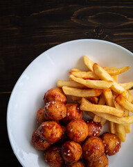 Spicy coated meatballs with spicy sauce served with fried potatoe fries. Korean style snacking.