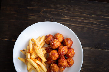 Spicy coated meatballs with spicy sauce served with fried potatoe fries. Korean style snacking.