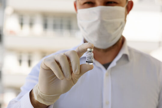 Doctor With White Gloves Holds Bottle With COVID-19 Vaccine. Concept Of Medicine, Clinical Trial And Treatment Due To SARS-CoV-2 Coronavirus. Blur Concept