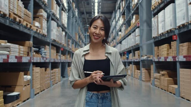 Portrait of attractive young Asia businesswoman manager smiling charmingly looking at camera hold digital tablet stand in retail shopping center. Distribution, Logistics, Packages ready for shipment.