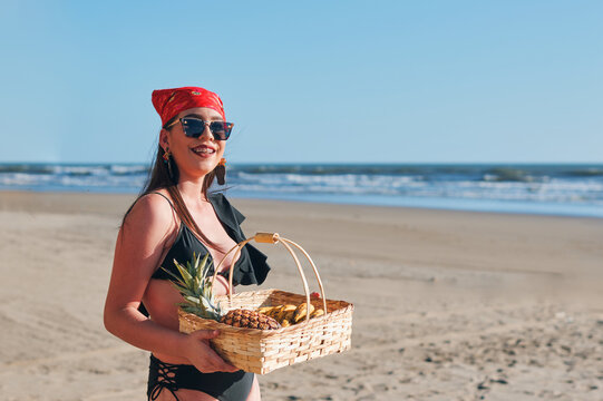 Beautiful woman in swimsuit holding basket with tropical fruits on the beach
