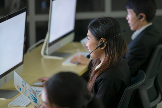 Asian smile woman wearing headphone headset and working with happy face and sevice mind in call center in front of computer screen in office at night. Overtime, late work and 24 hours service concept