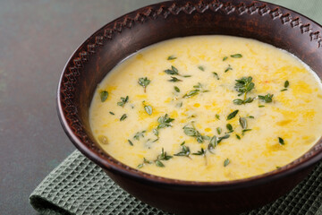 A bowl of cheese soup with thyme on a dark green background. Vegetarian food.