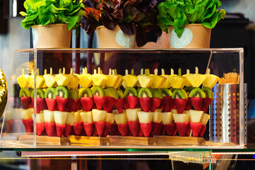 Chunks of exotic fruits on sticks, strawberries, pears, kiwis, and pineapples. Neatly displayed in a clear glass case.