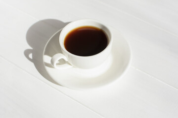 Espresso in a white cup on the table in bright sunlight. Creative composition with natural shadows. Modern breakfast. The concept of freshness of a summer morning. Minimalism, top view, white on white