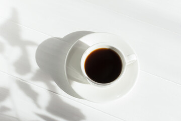 Espresso in a white cup on the table in bright sunlight. Creative composition with natural shadows. Modern breakfast. The concept of freshness of a summer morning. Minimalism, top view, white on white