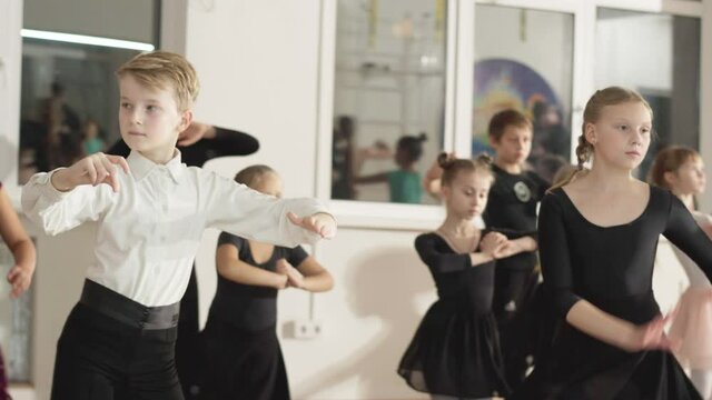 Group of Caucasian boys and girls dancing looking in mirror in dance studio. Skilled talented children rehearsing latin ballroom movements in dancing school. Art lifestyle.