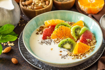 Healthy breakfast. Bowl of homemade granola with yoghurt, fresh fruit, nuts and chia seeds close-up on a dark stone tabletop.