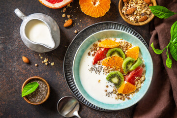Healthy breakfast. Bowl of homemade granola with yoghurt, fresh fruit, nuts and chia seeds on a dark stone tabletop. Copy space. Top view flat lay.