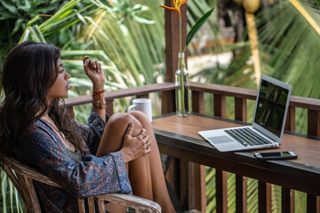 Portrait of young brunette woman freelancer working with laptop on balcony of tropical bungalow...
