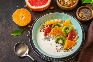 Healthy breakfast. Bowl of homemade granola with yoghurt, fresh fruit, nuts and chia seeds on a dark stone tabletop.