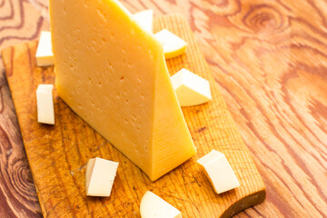 a large piece of cheese surrounded by small pieces on a wooden board
