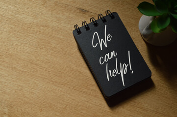Notebook written with text WE CAN HELP! over wooden background.