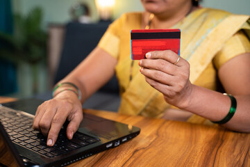 unrecognizable Indian woman hoilding credit card and entering card details into laptop for online e-commerce shopping or bill payment at home.
