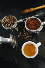 Close up Hot coffee espresso shot and a portafilter with coffee beans, a tamper portafilter with ground coffee on black table.