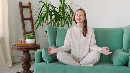 Young woman sit on couch in living room practice yoga relieve negative emotions at home