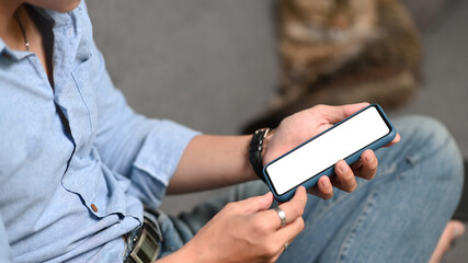 Cropped shot of casual young man using smart phone while sitting on couch with his cat in living room.