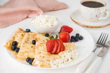 Traditional Russian thin pancakes with cottage cheese and berries in a plate on a white background