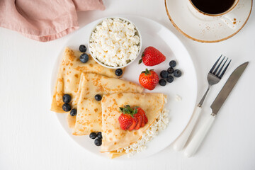 Traditional Russian thin pancakes with cottage cheese and berries in a plate on a white background