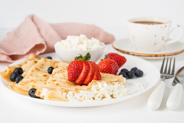 Traditional Russian thin pancakes with cottage cheese and berries in a plate on a white background
