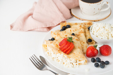 Traditional Russian thin pancakes with cottage cheese and berries in a plate on a white background, selective focus