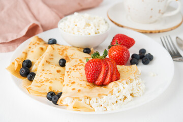 Traditional Russian thin pancakes with cottage cheese and berries in a plate on a white background,...