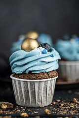 Several muffins or cupcakes with blue shaped cream and with blueberrieson at black table against a dark background. Rustic style copyspace.