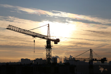 Silhouettes of construction cranes and residential buildings on sun background. Housing...