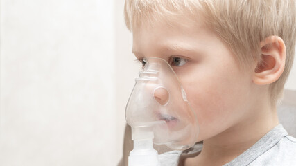 Close up portrait of blond boy taking inhalation for asthma prevention. Pale sick boy on a white background with a mask on his face. Treating colds and flu.