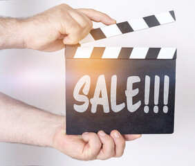 On a white background, a man holds a clapperboard in his hands on which it is written - SALE