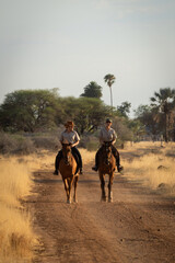 Two horsewomen ride side-by-side along dirt track