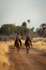 Naklejka premium Two horsewomen ride side-by-side along dirt track