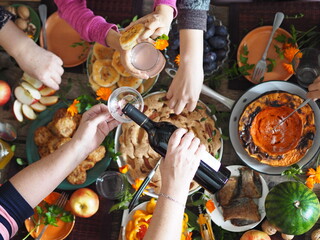 Thanksgiving day celebration concept. There is a lot of food on the wooden table.Guests pour red wine and take healthy homemade natural food with their hands.