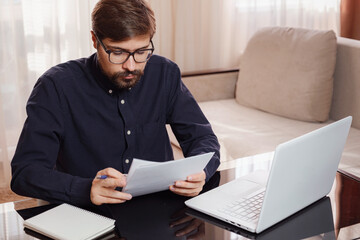 Entrepreneur works with a laptop and keeps a document in a home office