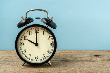 Black vintage alarm clock on a shabby wooden board background shows the time ten hours. Copy space.