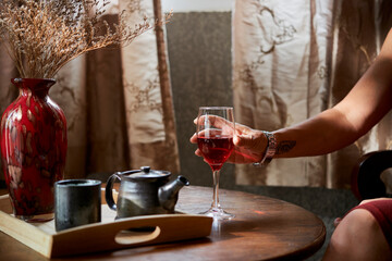 Hand of mature woman taking glass of red wine from coffee table
