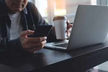 Casual business man, freelancer using mobile smartphone and drinking coffee during working on laptop computer from home office